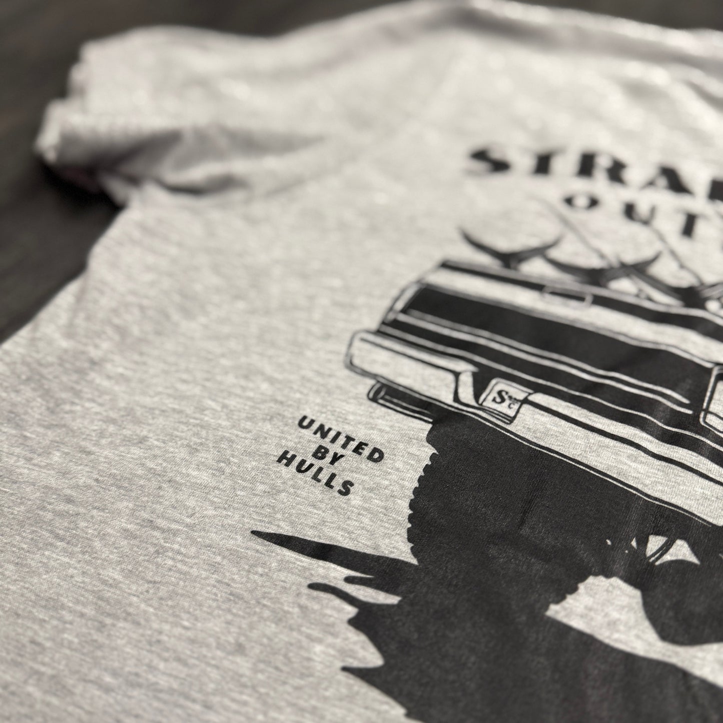 Gray t-shirt with black graphic design of a truck and text on a wooden surface